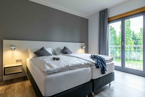 Un dormitorio moderno con una cama grande, mesitas de noche y un balcón con vistas a zonas verdes.