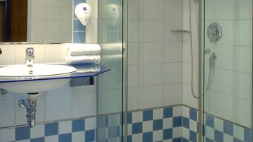 A bathroom with a glass-enclosed shower, a sink with a mirror, and a tiled floor.