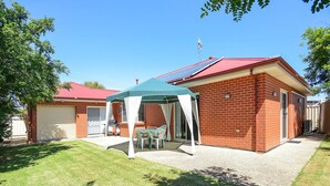 Une maison en briques avec un toit rouge, un patio couvert avec une table et des chaises, et un garage.