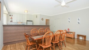 Un coin repas avec une table et des chaises en bois, une cuisine avec des meubles blancs et un ventilateur de plafond.