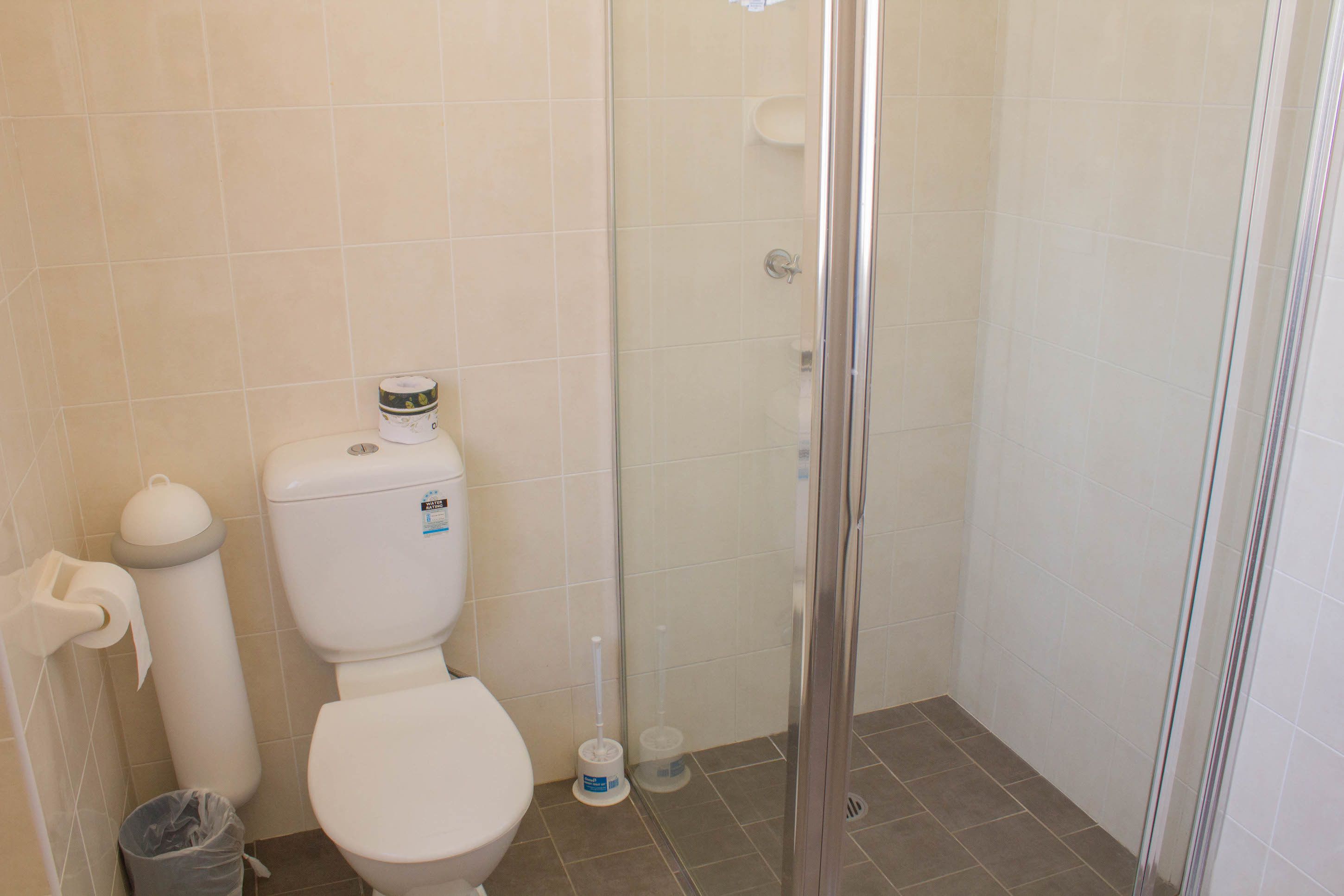 Une salle de bain équipée de toilettes, d’une poubelle et d’une cabine de douche.