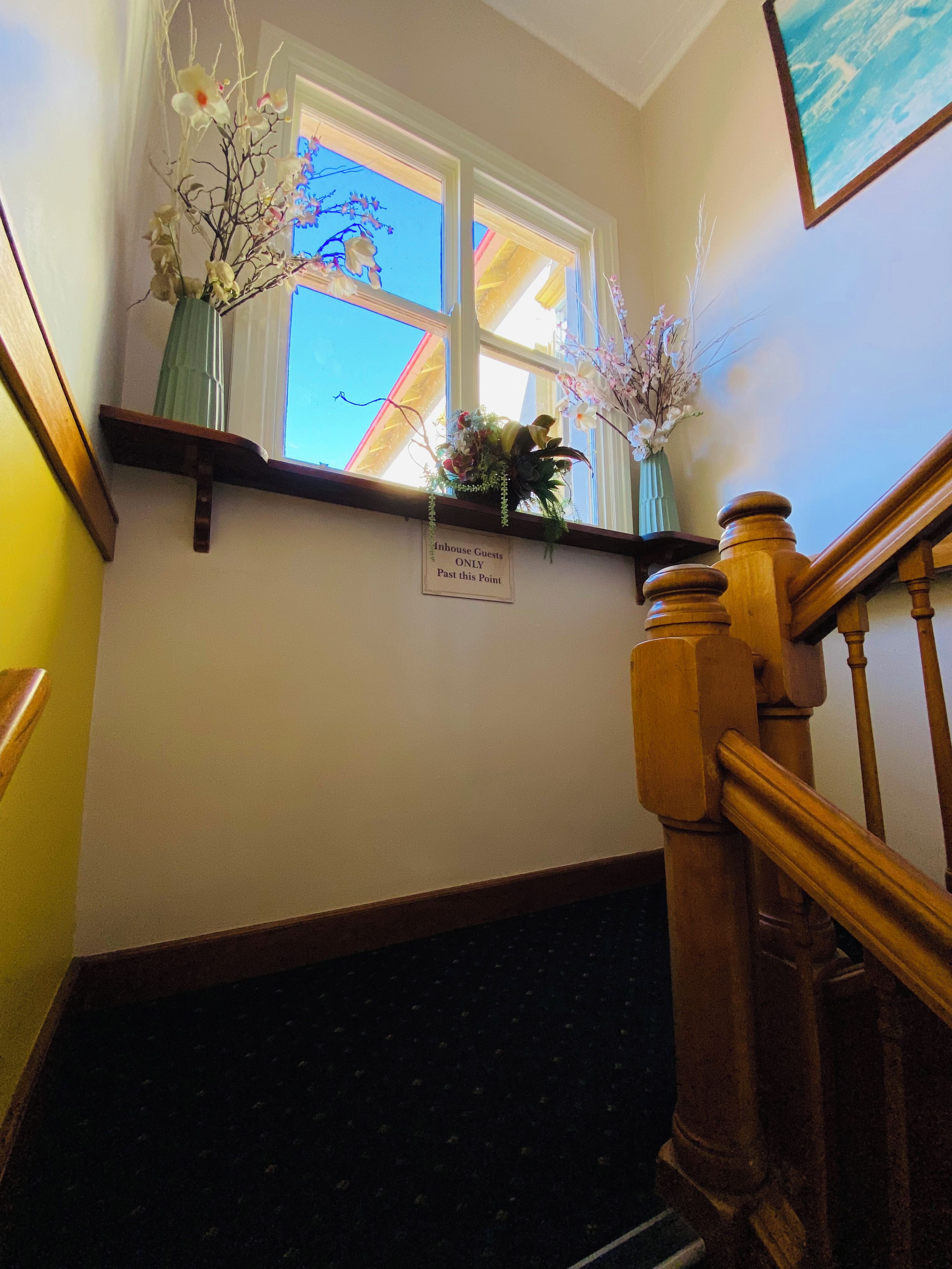 Una escalera con barandilla de madera, un letrero que indica 'Solo para huéspedes del hotel' más allá de este punto, y dos arreglos florales en un estante sobre la escalera.