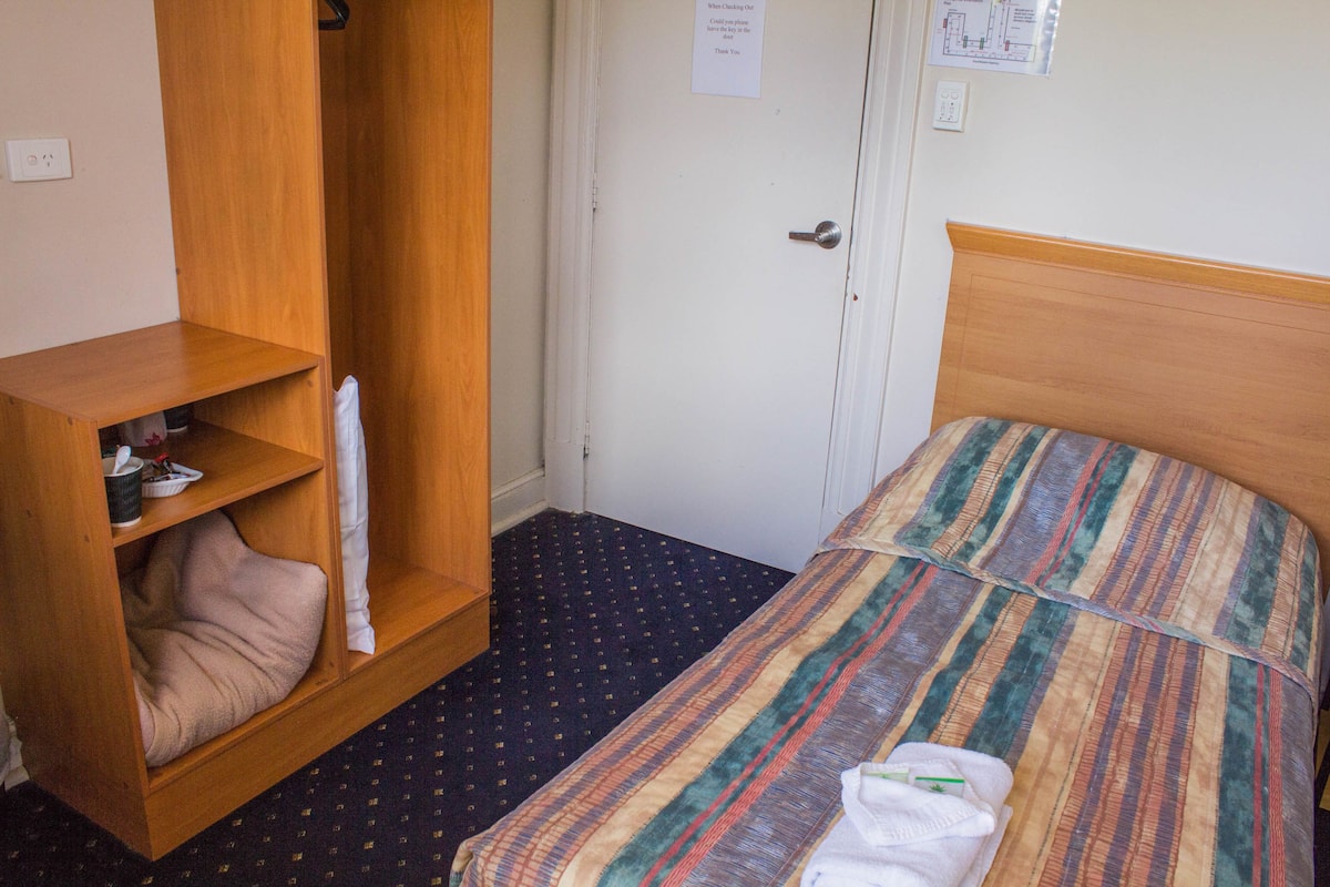 Ein Hotelzimmer mit einem Bett, einem Holzschrank, einem Regal mit einem Kopfkissen und einer Tür mit einem Schild.