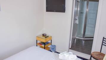 Hotelkamer met een bed, een klein houten nachtkastje met een afstandsbediening, een douchecabine van glas en een stoel.