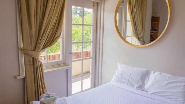 A hotel room with a bed, a window with curtains, a mirror, and a view of the outside.