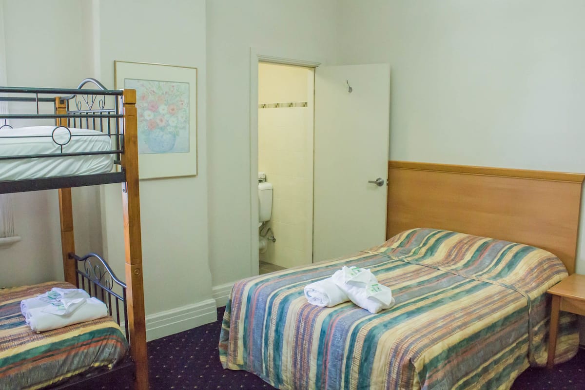 Ein Zimmer mit Etagenbetten, einem Einzelbett, einer Badezimmertür und einem gerahmten Bild an der Wand.