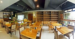Un café amplio con mesas y sillas de madera, una barra de café y estantes con diversos artículos.