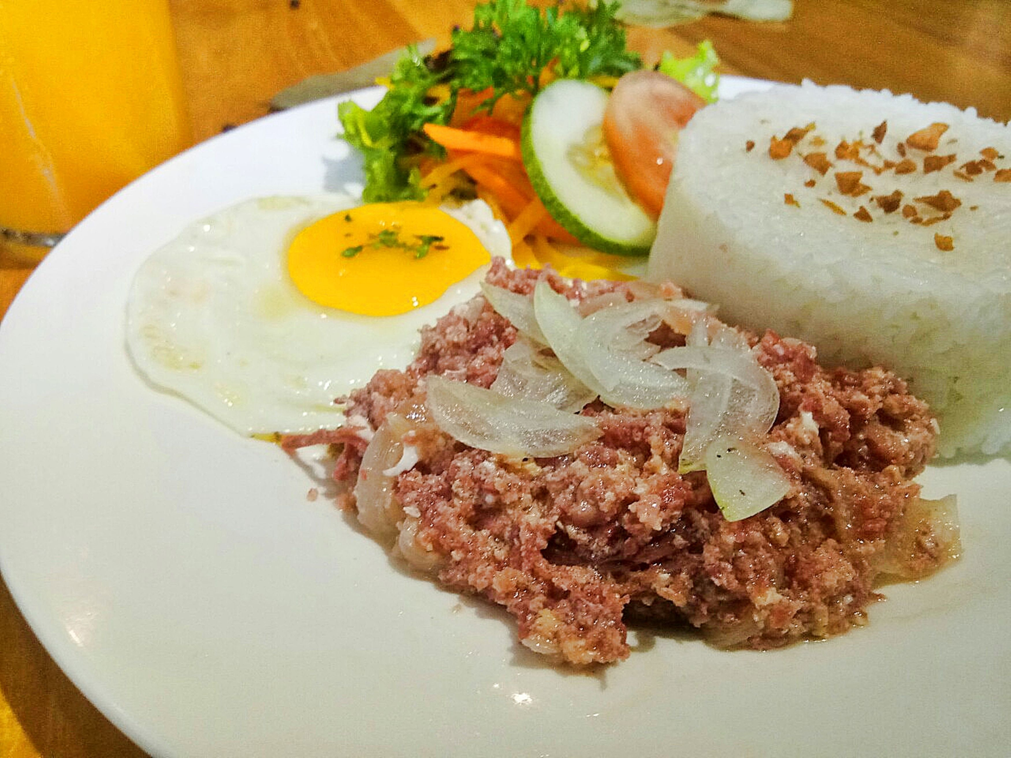 A plate with a fried egg, a meat dish, rice, and a side salad.