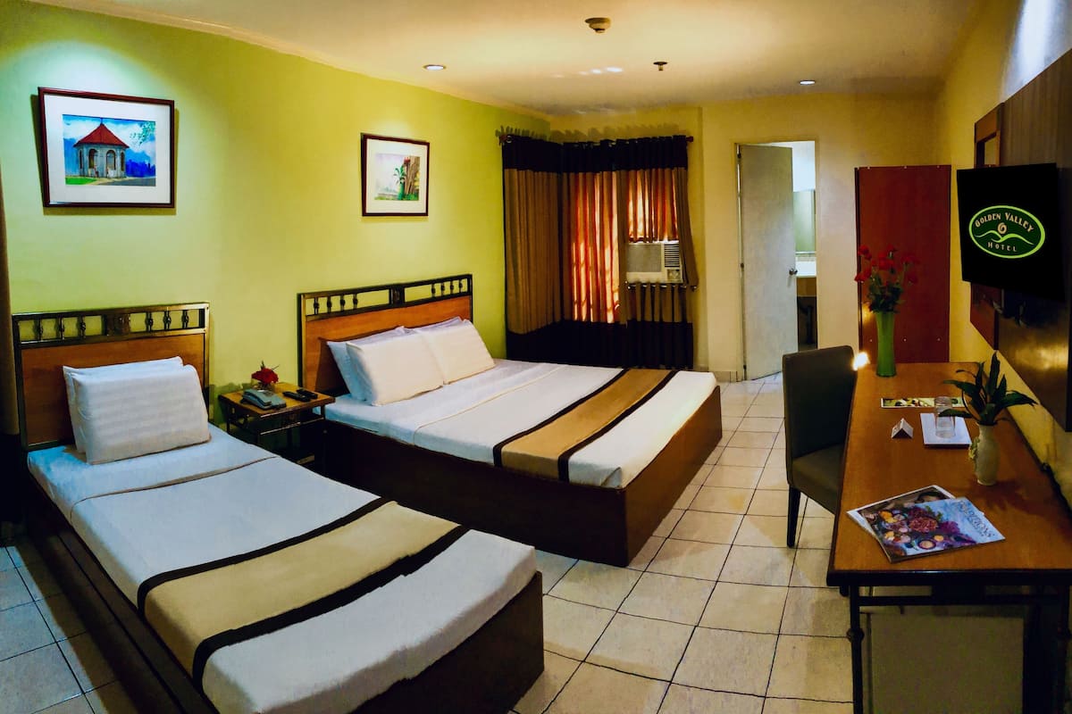 A hotel room with two beds, a desk, a chair, a TV, and two framed pictures on the wall.
