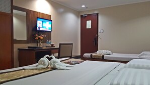 Quarto de hotel com duas camas, uma mesa com televisão, um vaso de flores e uma porta com um aviso.
