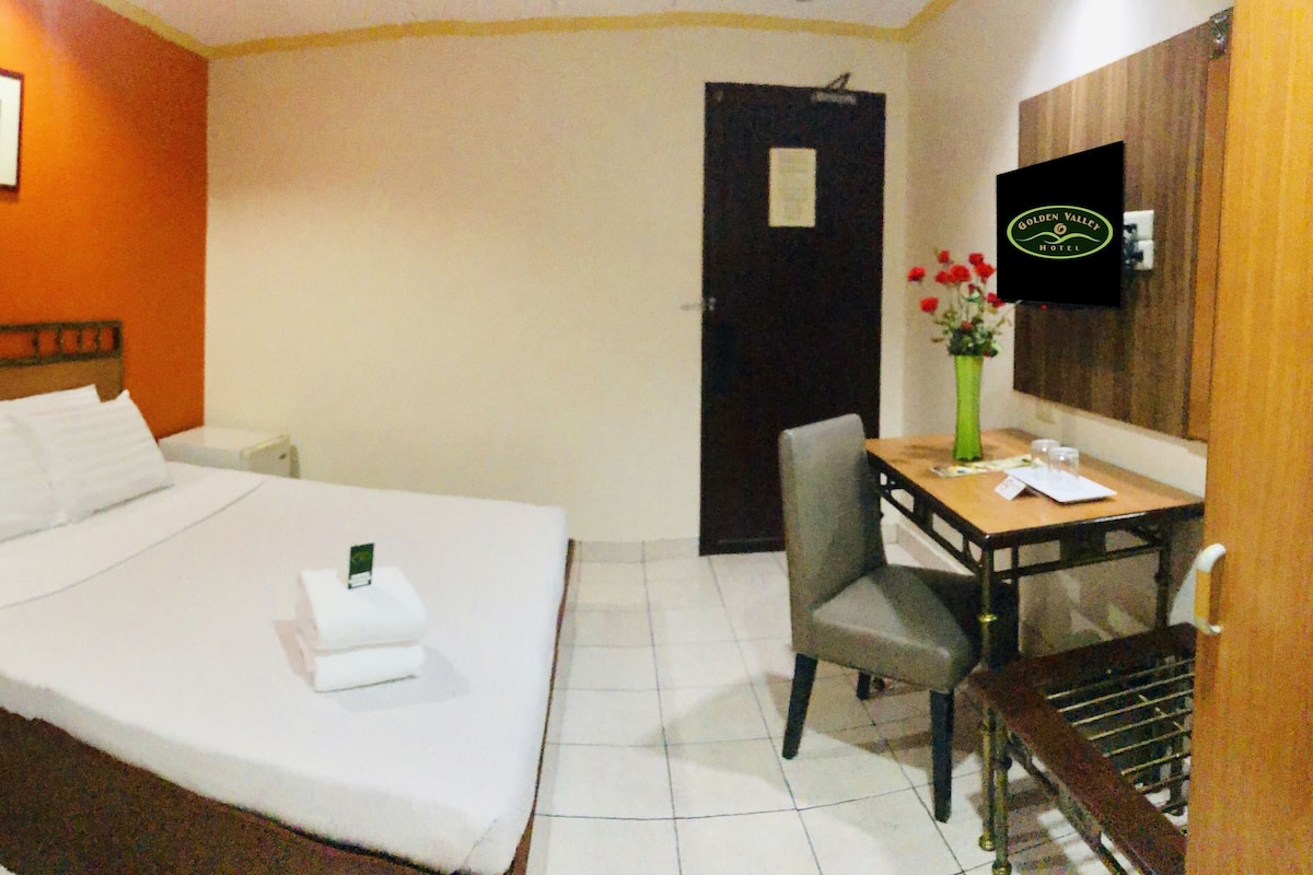 A hotel room with a bed, bedside table, chair, desk, and a mirror.