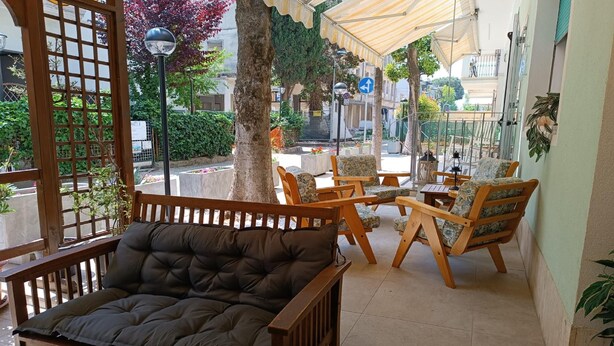 Een overdekt terras met houten meubels en een comfortabele bank.