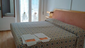 Een slaapkamer met een bed, een spiegel, een raam met gordijnen en een nachtkastje.