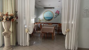 Een eetruimte met tafels en stoelen, een decoratieve vaas met bloemen en een muurschildering van een landschap.
