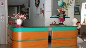 Een receptiebalie met een turquoise en oranje kleurenschema, een vaas met roze bloemen en een decoratief beeld op de toonbank.
