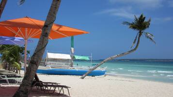 A beach with a boat, palm trees, and beach umbrellas.