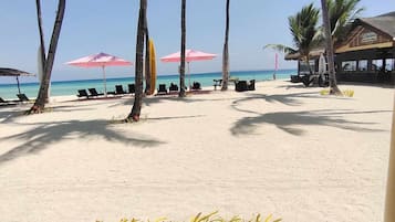 Una playa con palmeras, sillas de descanso y sombrillas.