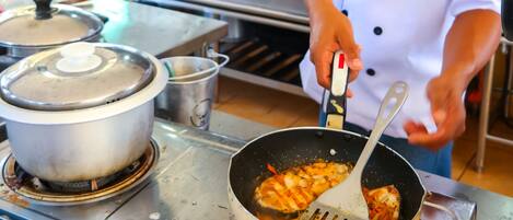 A chef in a white uniform with a name tag, cooking in a professional kitchen with stainless steel appliances and pots on the stove.
