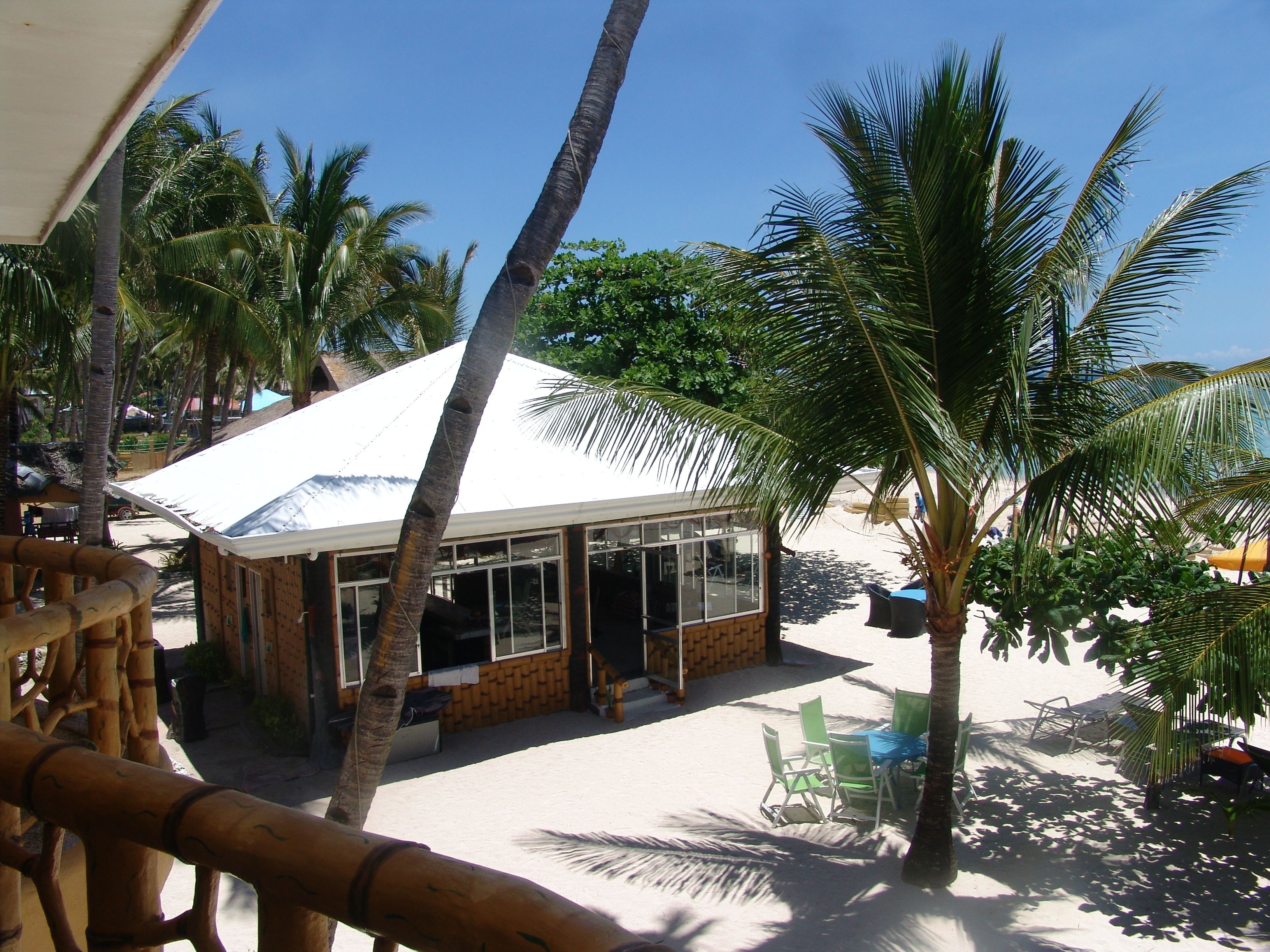 A beachside hut with a white roof, surrounded by palm trees and beach chairs.
