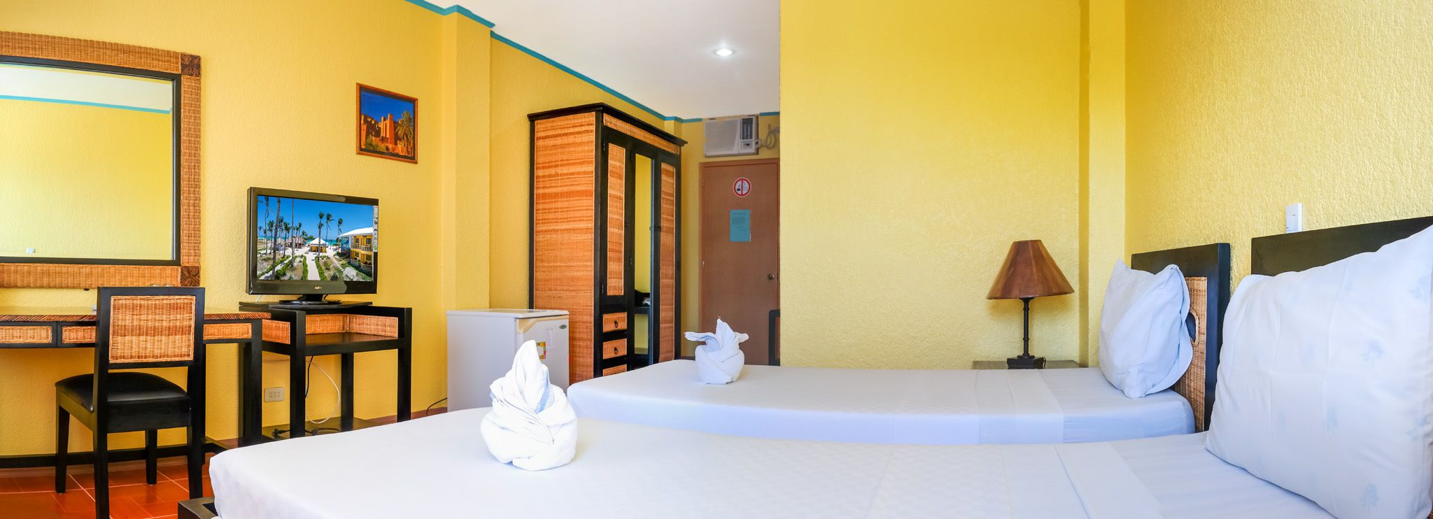 A hotel room with two beds, a desk, a television, and a door with a 'No Entry' sign.