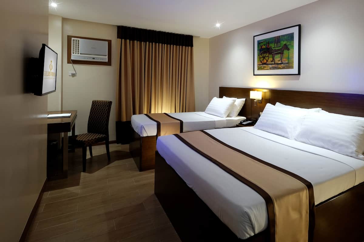 Habitación de hotel con dos camas, un escritorio, una silla, un equipo de aire acondicionado y un cuadro en la pared.