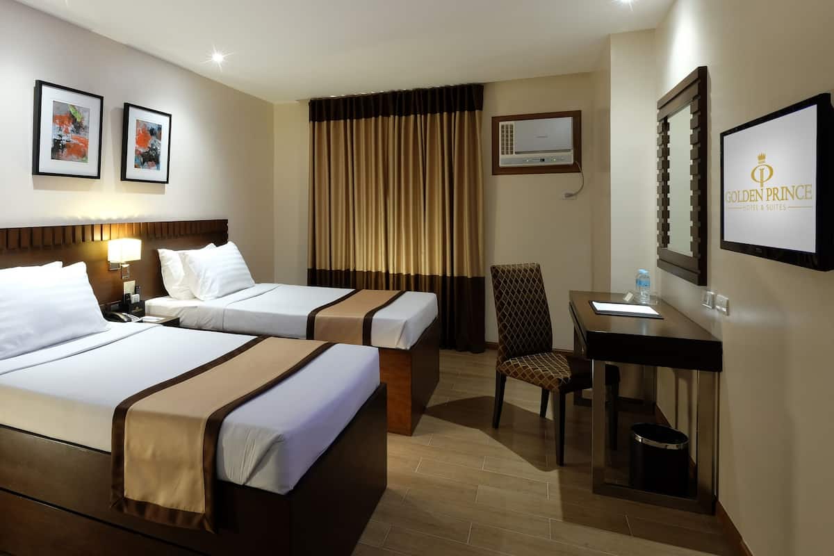 Habitación de hotel con dos camas, un escritorio, una silla, un televisor y cuadros en la pared.