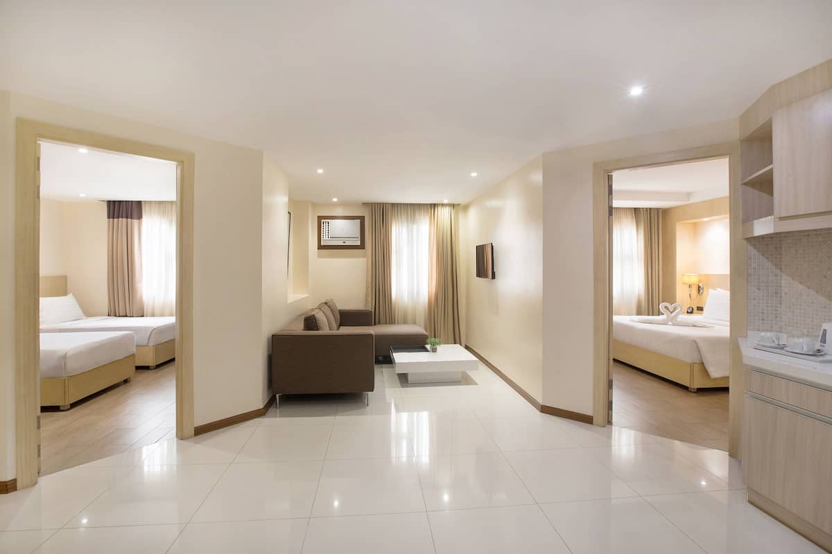 Habitación de hotel con dos camas, un sofá, una mesa de centro, un televisor y una kitchenette.