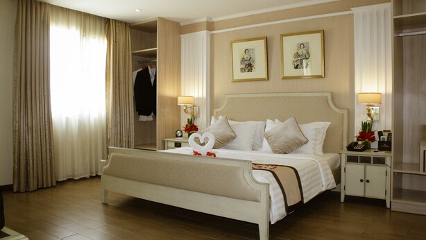 Une chambre d’hôtel avec un grand lit, deux tables de chevet, une armoire et une grande fenêtre avec des rideaux.