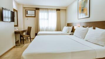 A hotel room with two beds, a desk, a chair, a television, and an air conditioning unit.