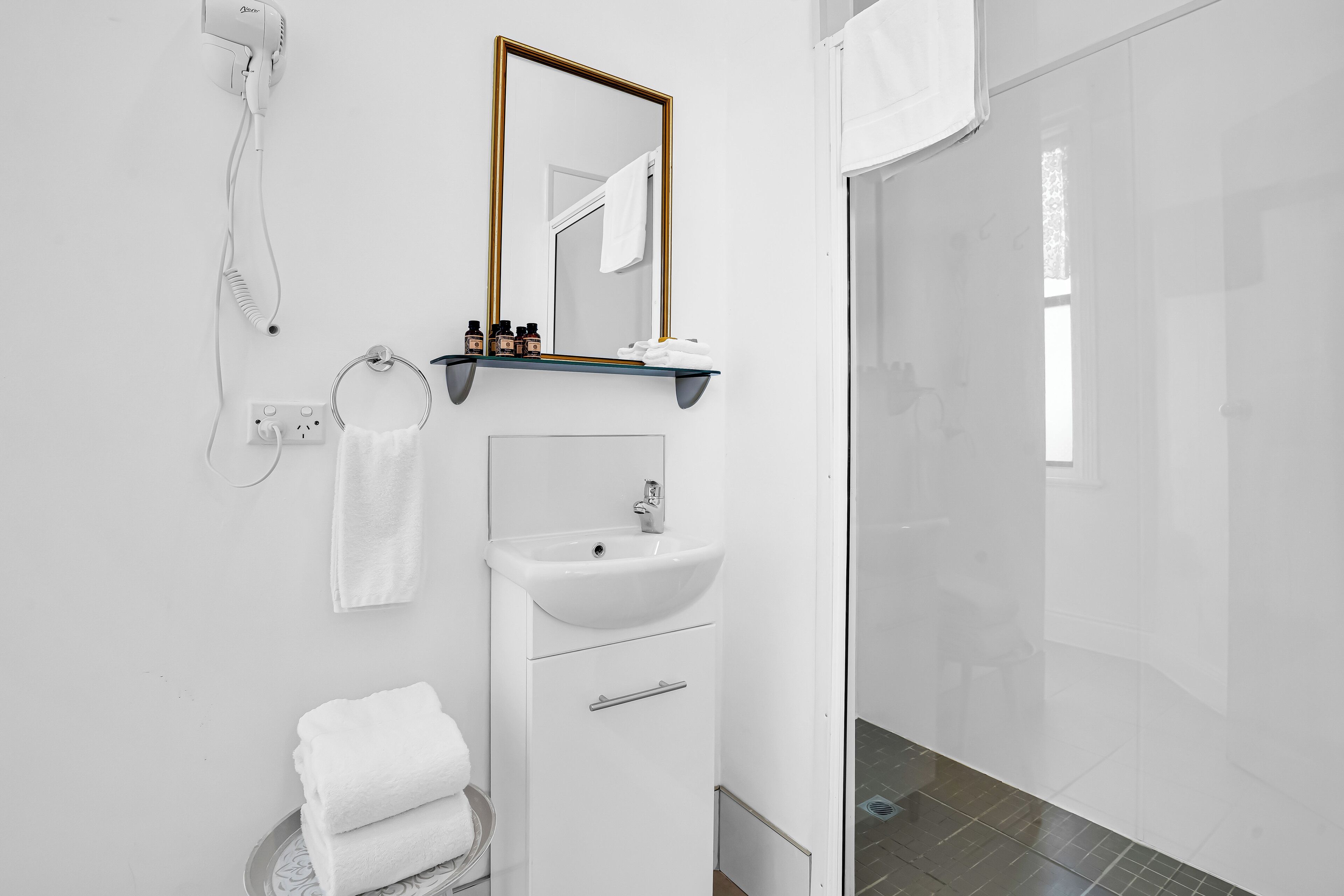 Un baño moderno con un lavamanos blanco, un espejo, un perchero para toallas y una zona de ducha.