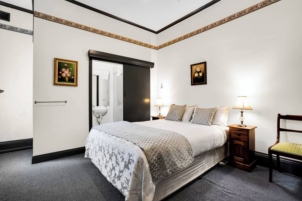 Ein ordentlich eingerichtetes Schlafzimmer mit einem großen Bett, Nachttischen, einem Sessel und zwei Wandleuchten.