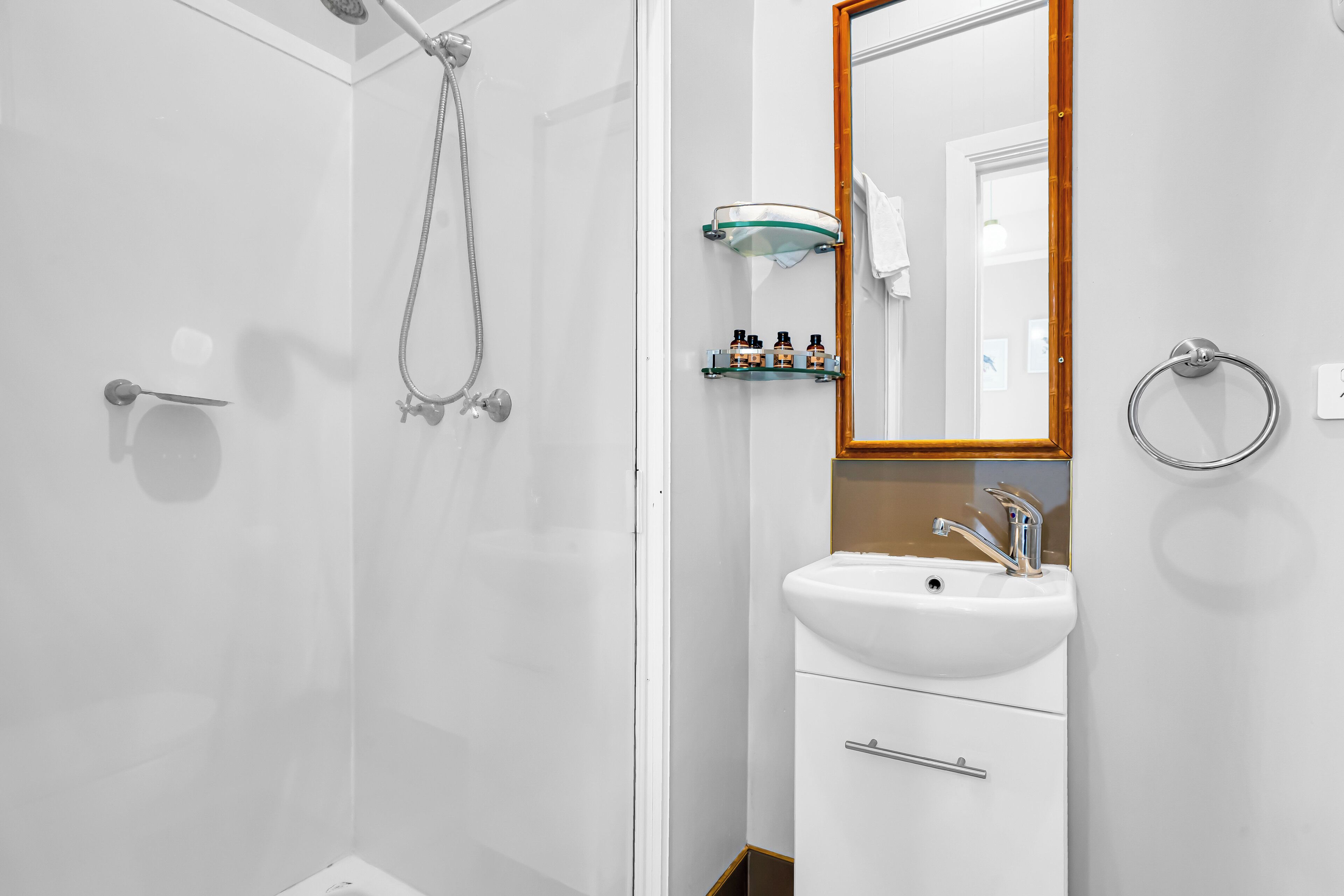 Un baño moderno con cabina de ducha de vidrio, un lavabo blanco y un espejo con marco de madera.