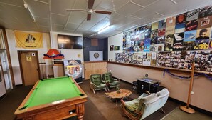 A pool room with a pool table, green chairs, a sofa, and a dartboard. - Bischoff Hotel (Waratah)
