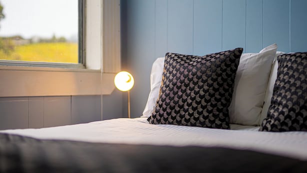 A bedroom with a bed, patterned pillows, a bedside lamp, and a window with a view of a field. - Bischoff Hotel (Waratah)