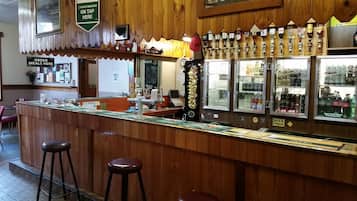 A bar area with a wooden counter, stools, and a variety of taps and bottles.