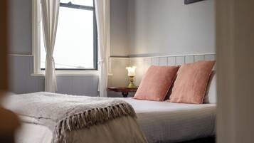Un dormitorio con cama, una mesita de noche con lámpara y una ventana con cortinas.