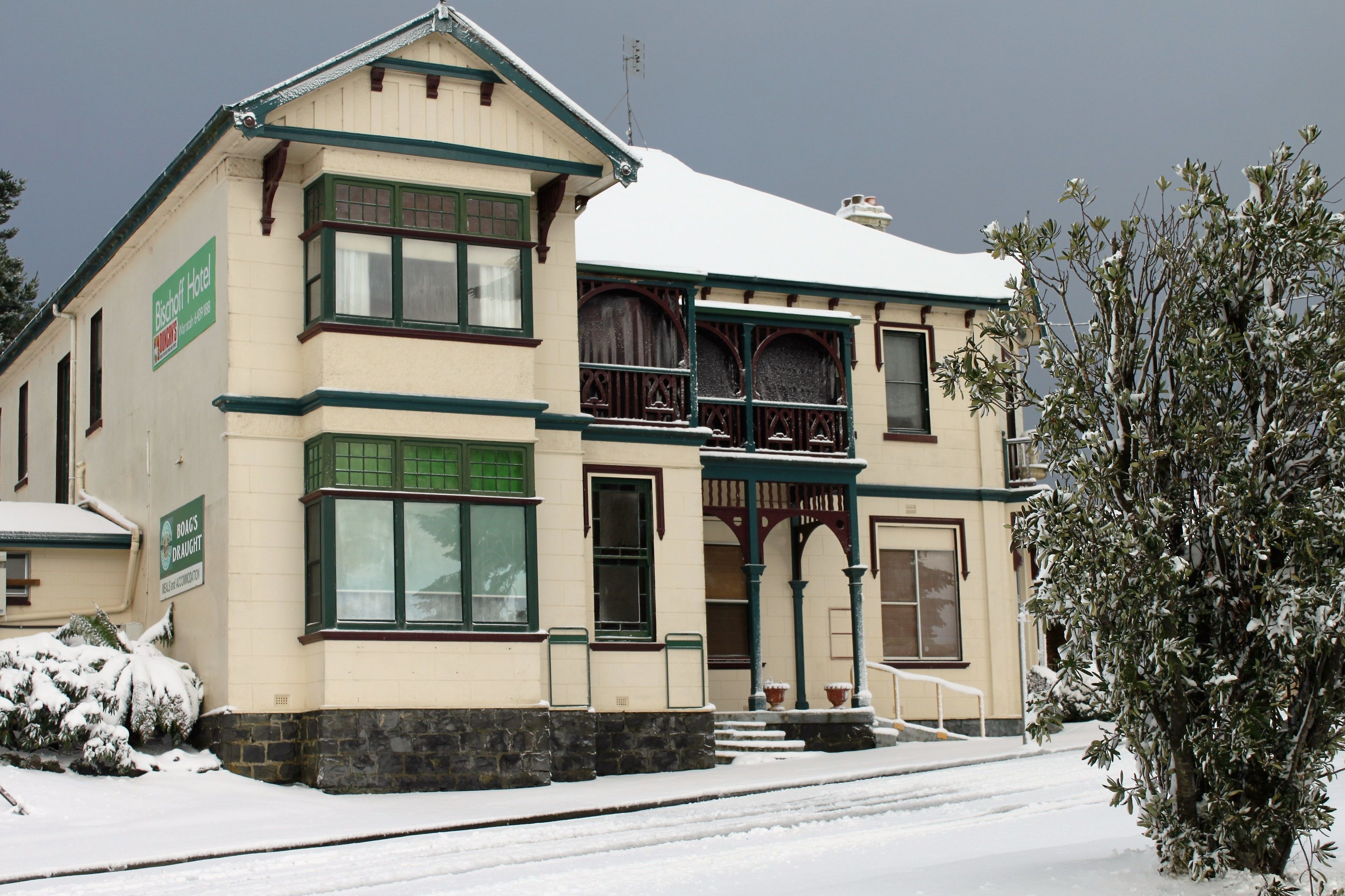 A two-story building with a snow-covered roof and a green-framed window.