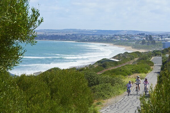A coastal path with cyclists, overlooking a beach and ocean.
