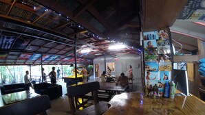 Un restaurante con mesas y bancos de madera, un techo alto con vigas a la vista y vistas al exterior.