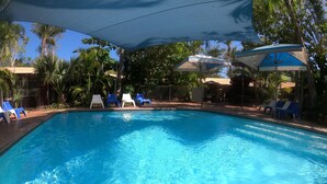 Una piscina con agua cristalina azul, rodeada de sillas reclinables azules y blancas, y con sombrillas que brindan sombra.