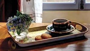 A tray with a cup of coffee and pastries on a table near a window with a view of a fountain and greenery outside. - Casa Valeri (Warburton)