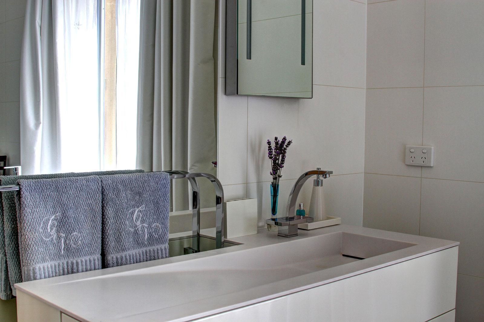 Un baño moderno con un lavamanos blanco grande, un espejo y una ventana con cortinas.