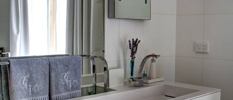 Un baño moderno con un lavamanos blanco grande, un espejo y una ventana con cortinas.