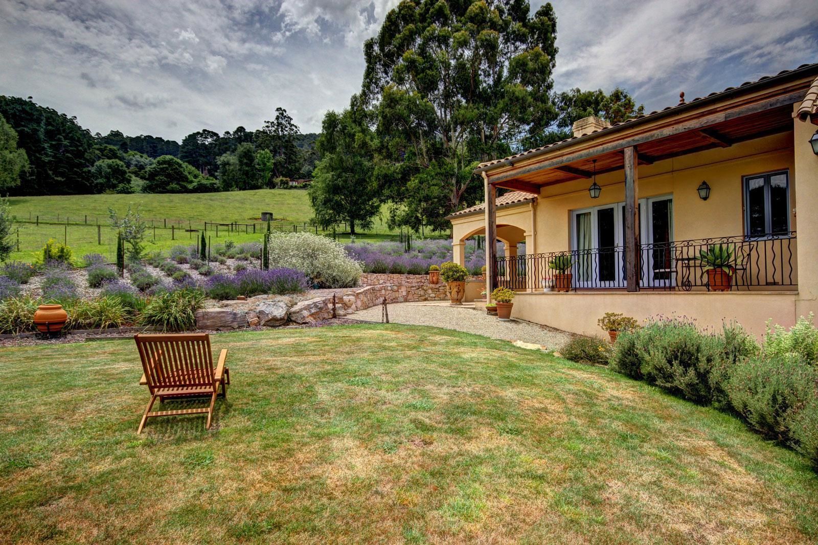 A house with a covered porch, a lawn, and a garden with various plants and a bench.