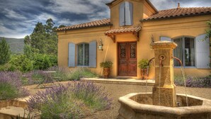 A Mediterranean-style house with a stone fountain, a wooden door, and a garden with lavender. - Casa Valeri (Warburton)