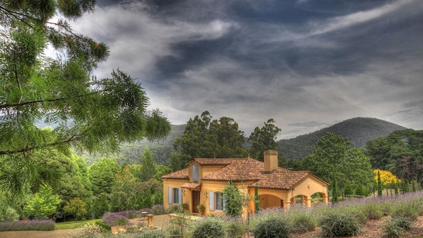 A house with a tiled roof, surrounded by a garden with various plants and a mountain in the background. - Casa Valeri (Warburton)