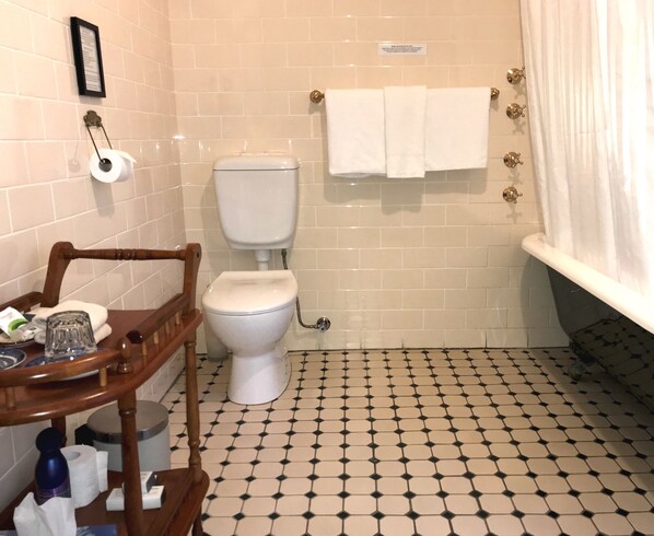 Un baño con inodoro, una silla de madera, una mesita con artículos de aseo, un perchero con dos toallas y un suelo estampado.