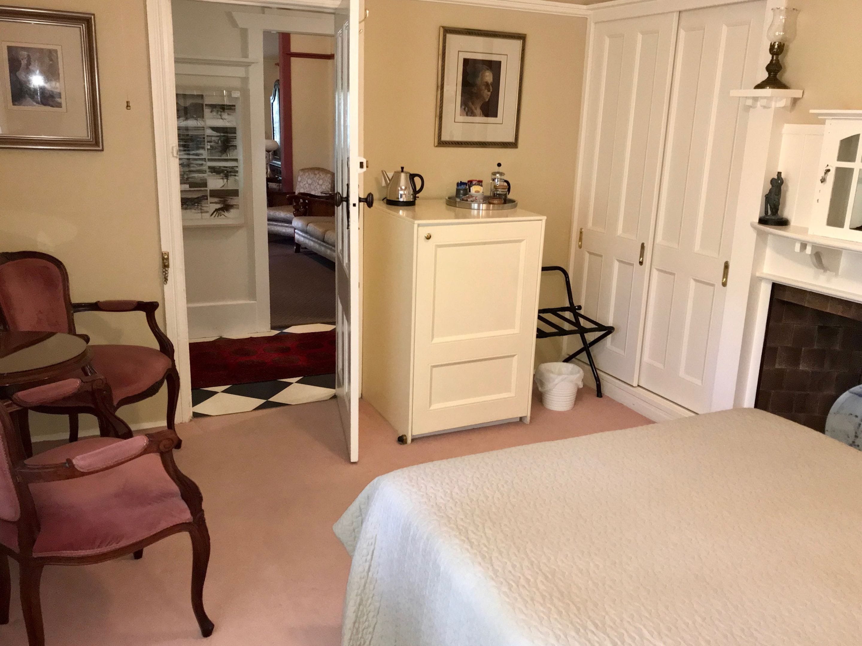 A bedroom with a bed, a wooden chair, a cabinet, a fireplace, and a door leading to another room.