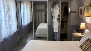 Een hotelkamer met een groot bed, een badjas hangend aan de deur, een bedlamp en een brandblusser aan de muur.