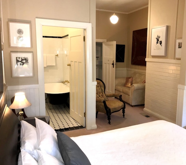 A bedroom with a bed, a chair, a lamp, and a bathroom visible through an open door. - The Chalet Guesthouse and Studio (Medlow Bath)